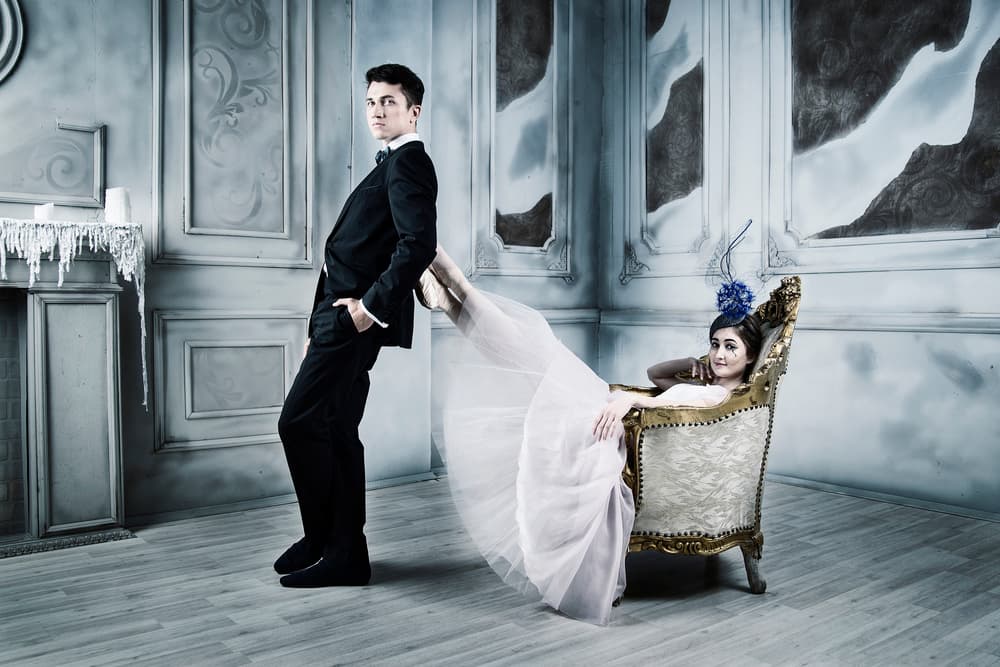melancholy. man stands in the loft leaning on the legs of a ballerina sitting in an armchair by Alexandr — canvas wall art